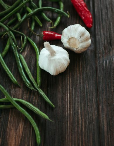pexels photo 5644931 5644931 Close-up of garlic, green beans, and red chili peppers on a rustic wooden surface.